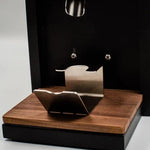 A close-up of a coffee machine with a black body, dark wood base and side panel, and stainless steel drip tray and portafilter holder.