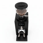 A black electric coffee grinder filled with roasted coffee beans, featuring a clear bean hopper, a digital control panel, and a metal chute on a white background.
