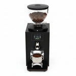 A close-up of a black coffee grinder with a clear bean hopper filled with coffee beans, a digital display screen, and a metal portafilter filled with ground coffee below.